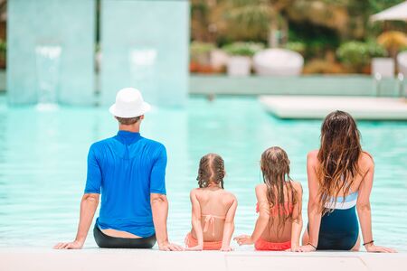 Happy family of four in outdoors swimming pool