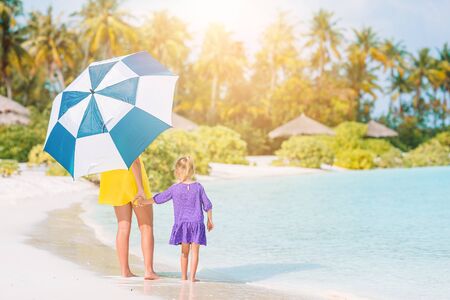 Mother and little daughter on the beach with umbrella to hide from sunの写真素材