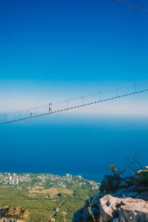 Girls crossing the chasm on the rope bridge. Black sea background, Crimea, Russia