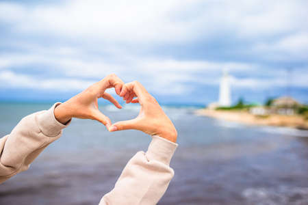 Female hands in the form of heart against the lighthouse
