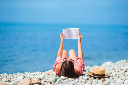 Young woman reading book during tropical white beachの写真素材