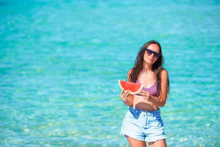 Happy girl having fun on the beach and eating watermelon