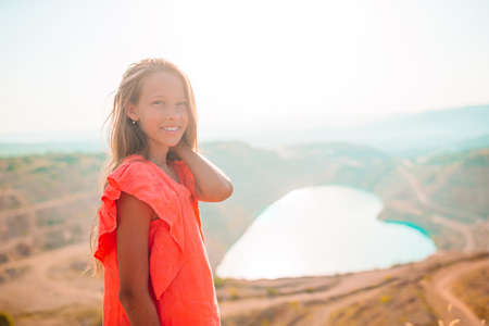 Little girl near the lake at the day time with amazing nature on background