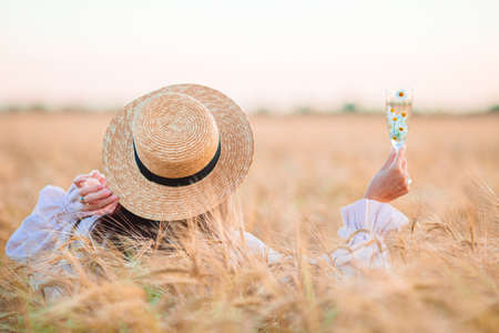 Back view of girl in wheat field. Beautiful woman in dress in a straw hat with ripe wheat in handsの写真素材