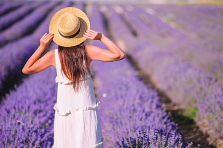 Woman in lavender flowers field at sunset in white dress and hatの写真素材