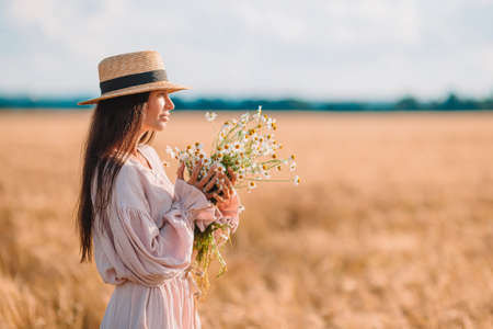Back view of girl in wheat field. Beautiful woman in dress in a straw hatの写真素材