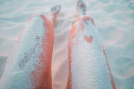 Womans feet on the white sand beach in shallow waterの写真素材