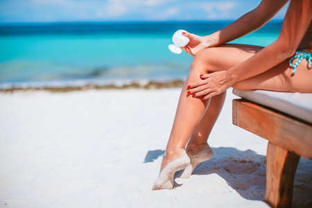 Beautiful young woman holding a suncream lying on tropical beachの写真素材