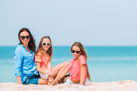 Adorable little girls and young mother on tropical white beach