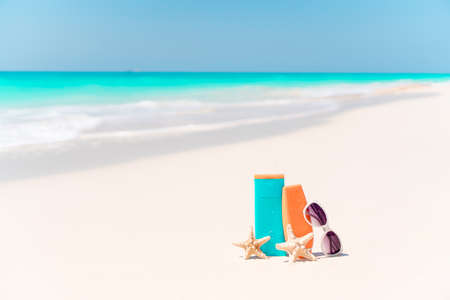 Suncream bottles, goggles, starfish and sunglasses on white sand beach background ocean