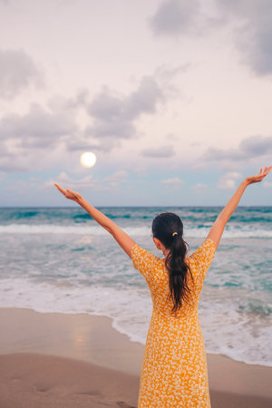 Happy woman enjoying beautiful sunset with big full moon on the beach