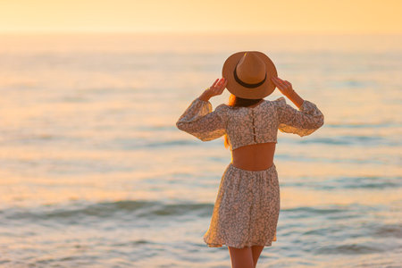 Young beautiful woman at straw hat on the beach at sunsetの写真素材