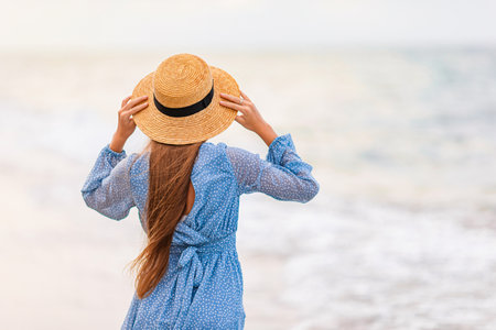 Beautiful teenager girl on tropical seashore at sunset. Beautiful little girl in dress at beach look at the sea.の写真素材