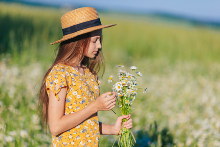 Portrait of girl in a yellow dress and straw hat on a chamomile field in summerの写真素材