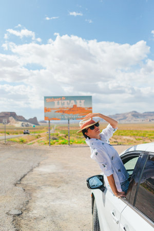 Beautiful woman on her trip by the car. Welcome to Utah road sign. Large welcome sign greets travels in Monument Valley, Utahの写真素材
