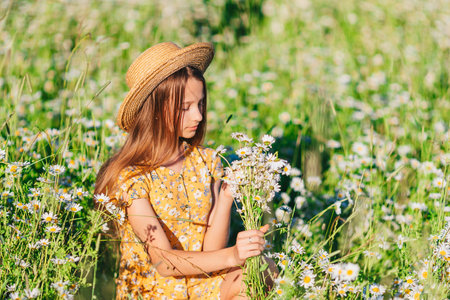 Portrait of girl in a yellow dress and straw hat on a chamomile field in summerの写真素材