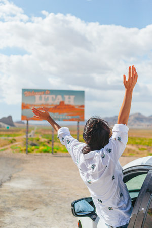 Beautiful woman on her trip by the car. Welcome to Utah road sign. Large welcome sign greets travels in Monument Valley, Utahの写真素材