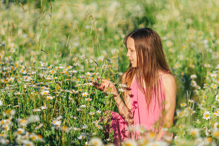 Portrait of girl in dress and straw hat on a chamomile field in summerの写真素材
