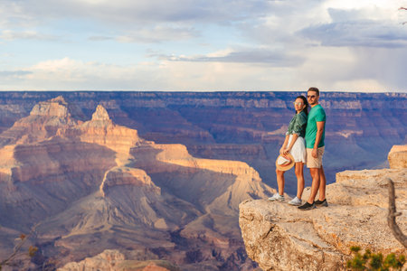 Happy couple on a steep cliff taking in the amazing view over famous Grand Canyon on a beautiful sunset, Grand Canyon National Park, Arizona, USAの写真素材