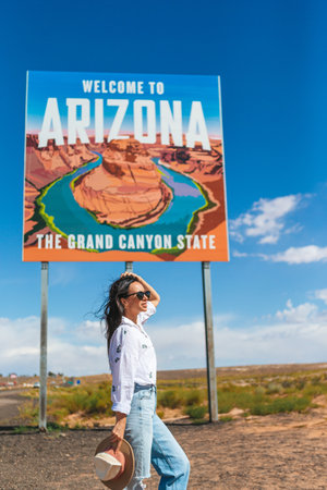 Beautiful woman on her trip to the USA on the background of Welcome to Arizona State border sign right in the Paje Canyon, USAの写真素材