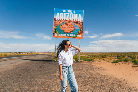 Beautiful woman on her trip to the USA on the background of Welcome to Arizona State border sign right in the Paje Canyon, USAの写真素材