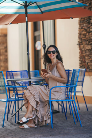 Beautiful woman typing a message in outdoor summer cafeの写真素材