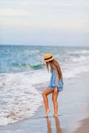 Adorable young girl with beautiful long hair enjoy tropical beach vacation. The girl on the seashore at sunsetの写真素材