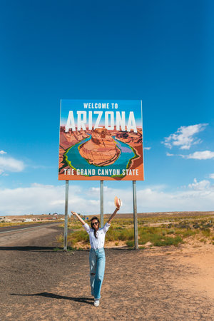 Beautiful woman on her trip to the USA on the background of Welcome to Arizona State border sign right in the Paje Canyon, USAの写真素材