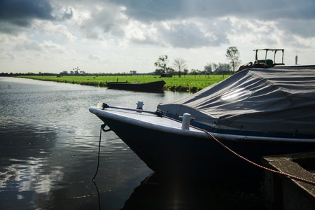 boat standing on the water attached to the shore and covered with a special material before it starts to rain water dark light boat tighten the skyの写真素材