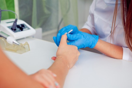 Closeup shot of a woman in a nail salon receiving a manicure by a beautician with nail file. Woman getting nail manicure. Beautician file nails to a customerの写真素材