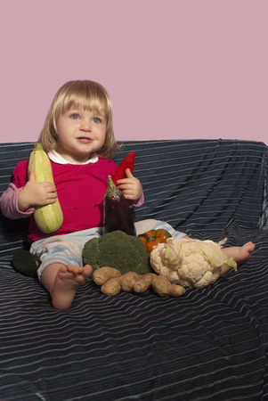 Baby girl sitting surrounded by vegetablesの写真素材