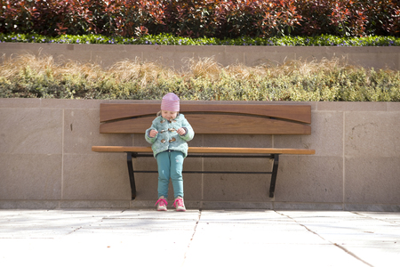 Little girl is trying to sit on a benchの写真素材