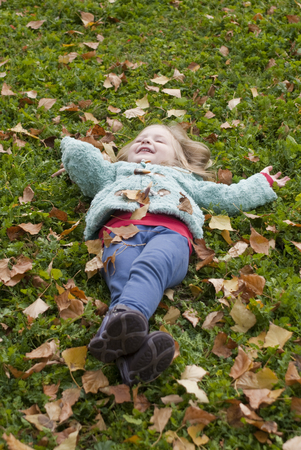 Pretty little girl lying on the grass playing with leavesの写真素材