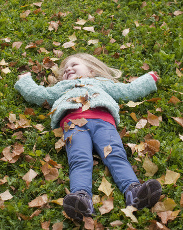 Pretty little girl lying on the grass playing with leavesの写真素材