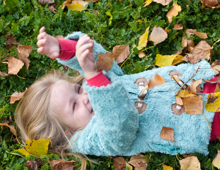 Pretty little girl lying on the grass playing with leavesの写真素材