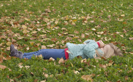 Pretty little girl lying on the grass playing with leavesの写真素材