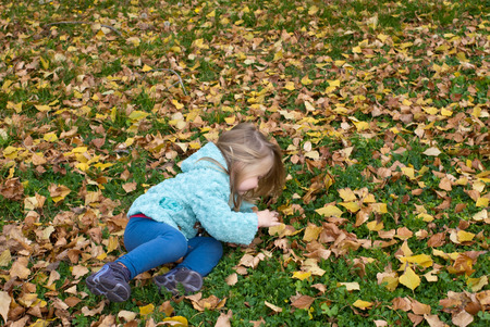 Pretty little girl sitting on the grass playing with leavesの写真素材