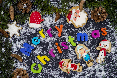 Colorful christmas title surrounded with snow and cookies on black backgroundの写真素材