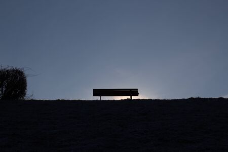 Silhouette of a empty bench and a bush on a hill and a clear skyの写真素材