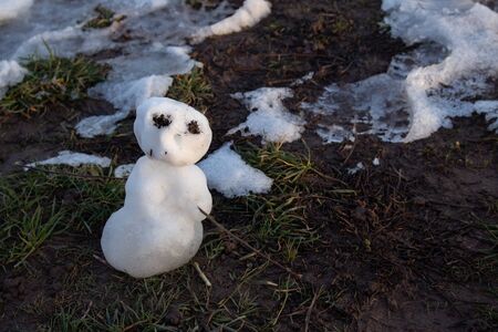 Last miniature snowman standing in mud and grass, melting in the evening sun in springの写真素材