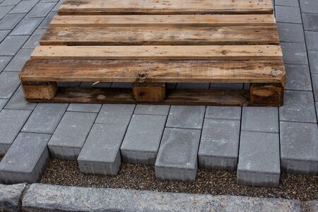 Concrete paver blocks laid beside a building, leaving space to the curbstone, a empty wooden pallet is laying on the new pavewayの写真素材