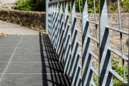 Slanted view of a metal railing on a bridge casting shadows with natural stone walls in the background, focus on foregroundの写真素材