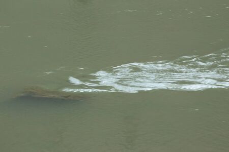 Rock in the water of a river creating waves on the surface of the currentの写真素材