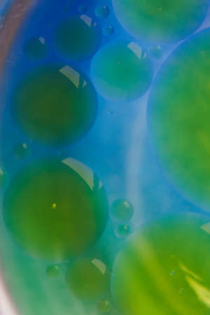 Blurred soft focus of oil spheres in water with color transition from green to blue tones for colorful backgroundの写真素材