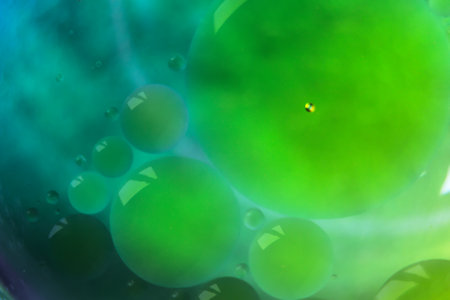 Blurred soft focus of oil spheres in water with color transition from green to blue tones for...