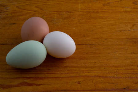 White, brown and green Araucana chicken egg laying on a wooden cutting board with copy spaceの写真素材