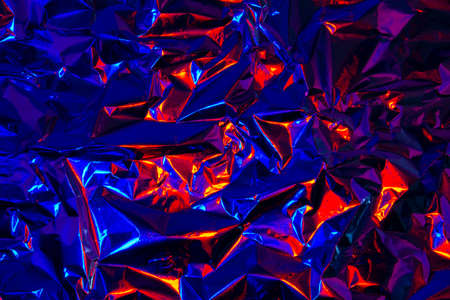 Abstract red and blue aluminum wrinkled foil background texture reflecting red and blue lightの写真素材