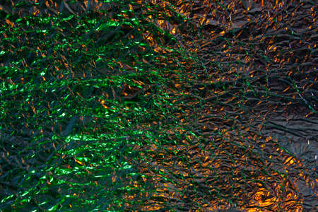 Abstract gold and green aluminum wrinkled foil background texture reflecting green and golden yellow...