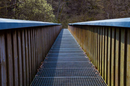 Footbridge with iron grating floor and wooden railing crossing a river