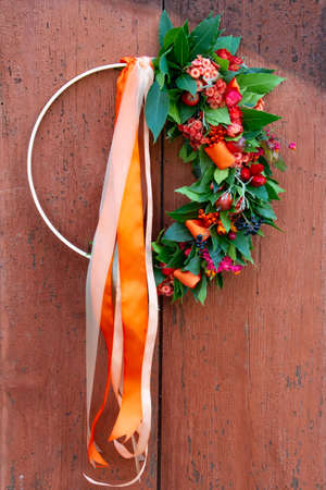 Wreath made out of laurel and dry flowers with ribbons hanging on a wooden doorの写真素材